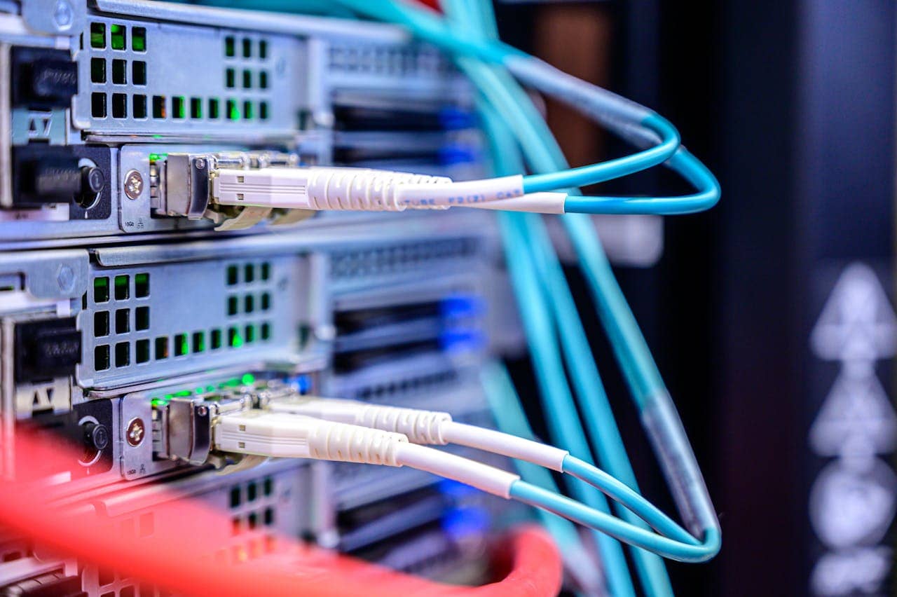 Close-up of network cables plugged into ports on the back of server units in a data center, with indicator lights visible.